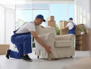 Professional movers from full-service interstate removals company efficiently packing up a cozy living room, with the homeowner relaxing on the couch.